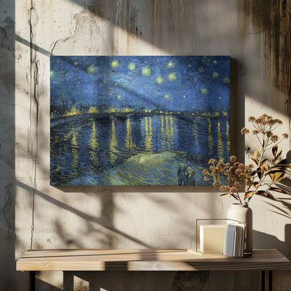A framed print of Vincent van Gogh's painting, 'Starry Night Over the Rhône'. The artwork features a deep blue night sky filled with glowing yellow stars above a city skyline. The city lights and stars cast long, shimmering yellow reflections on the dark blue water of the river. In the foreground, two small figures of a couple are seen walking along the riverbank. Artwork