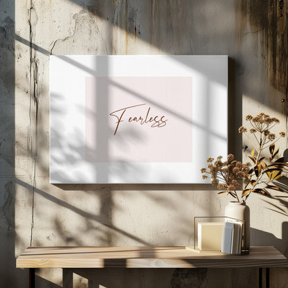 A framed artwork featuring the word 'Fearless' in a flowing brown script font on a pale pink background. The piece is surrounded by a white mat and a textured silver frame. Wall Art