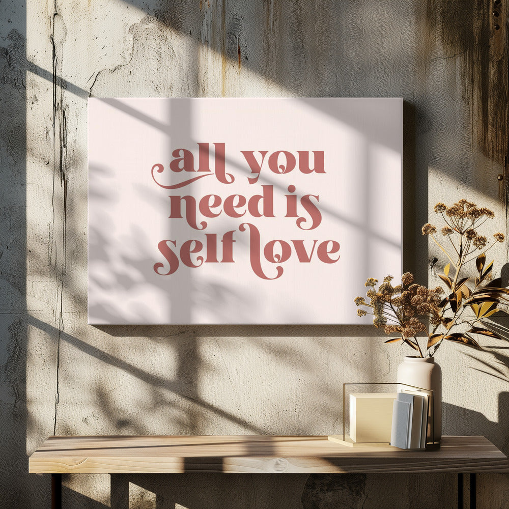 A framed art print with the phrase 'all you need is self love' in a stylish, dusty rose serif font on a light pink background. The artwork is enclosed in a simple silver frame. Poster