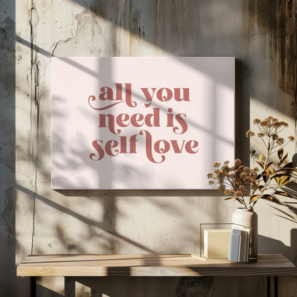 A framed art print with the phrase 'all you need is self love' in a stylish, dusty rose serif font on a light pink background. The artwork is enclosed in a simple silver frame. Poster