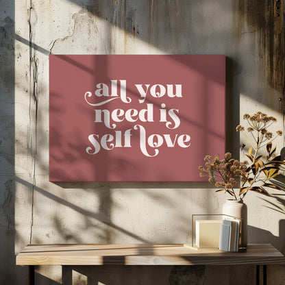 A framed art print with a dusty rose background. In the center, the phrase 'all you need is self love' is written in a creamy white, stylized, retro font. The artwork is enclosed in a simple silver frame. Decor