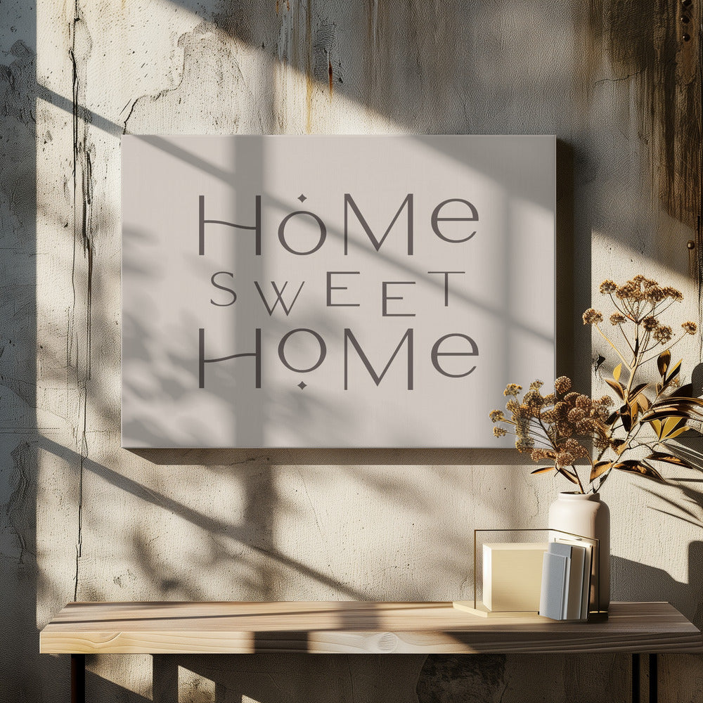 A minimalist wall art piece with the words 'Home Sweet Home' in a dark gray, stylized sans-serif font against a light beige background, all housed within a simple silver frame. Decor