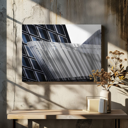 An abstract architectural photograph, framed in silver, showing a dynamic contrast between two modern building facades. In the background, a dark building features a grid of diamond-shaped windows with white frames, while a structure in the foreground creates a wave of fine, parallel white vertical lines against the sky and the other building. Print