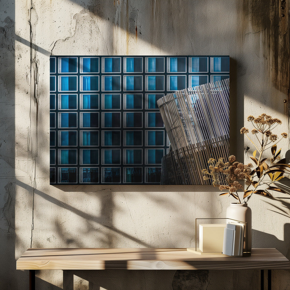 An architectural abstract photograph featuring a modern building facade with a grid of blue and black square windows, contrasted by a curved, slatted structure in the foreground, all enclosed in a silver frame. Wall Art
