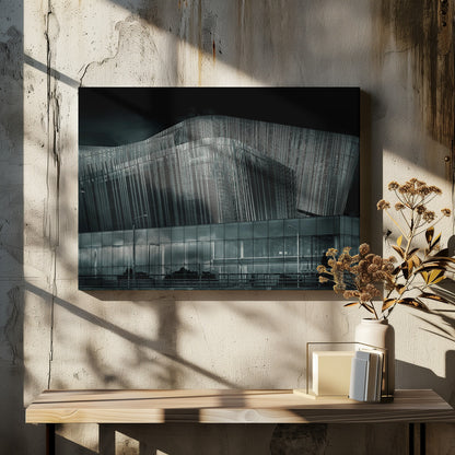 A dramatic black and white photograph of a modern building with a unique, wave-like facade made of vertical fins. The lower level is made of glass, reflecting the sky and streetlights. The entire image is presented in a silver frame. Artwork