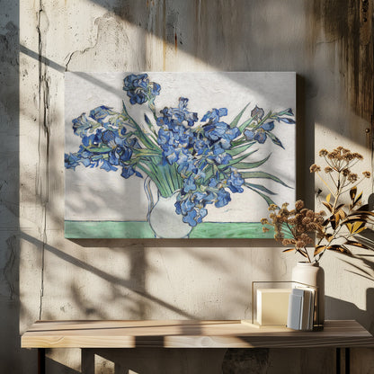 A framed print of Vincent van Gogh's famous painting 'Irises'. It features a large bouquet of vibrant blue iris flowers with long green leaves, arranged in a simple white pitcher. The background is a textured off-white wall, and the pitcher rests on a light green surface. The painting is in the post-impressionist style with thick, visible brushstrokes. Wall Art