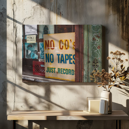 A weathered yellow sign in a record store window reads 'NO CD'S NO TAPES JUST RECORDS' in bold lettering. Behind the sign, vintage album covers and other posters are visible in the shop's display, next to a rustic green and brown door frame. Decor