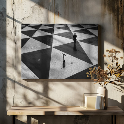 A high-angle, black and white photograph of a man in a coat and fedora walking away across a vast plaza with a geometric pattern of black and light gray triangles. An electric scooter stands alone in the foreground, creating a sense of solitude and contrast. The image is presented within a silver frame. Decor