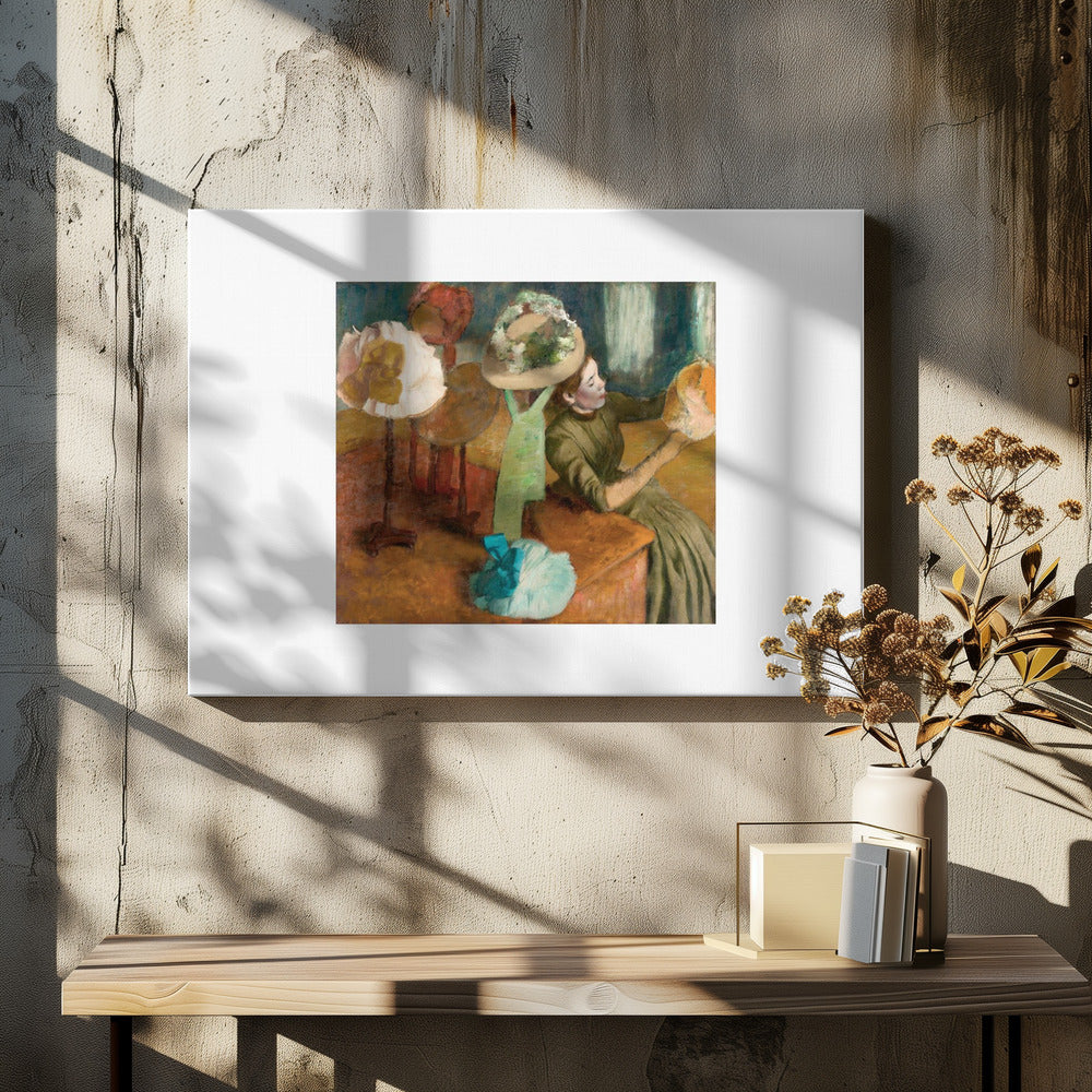 A framed print of Edgar Degas's Impressionist painting 'The Millinery Shop,' showing a woman in a green dress examining a hat in a shop filled with various fashionable hats on display stands. Print