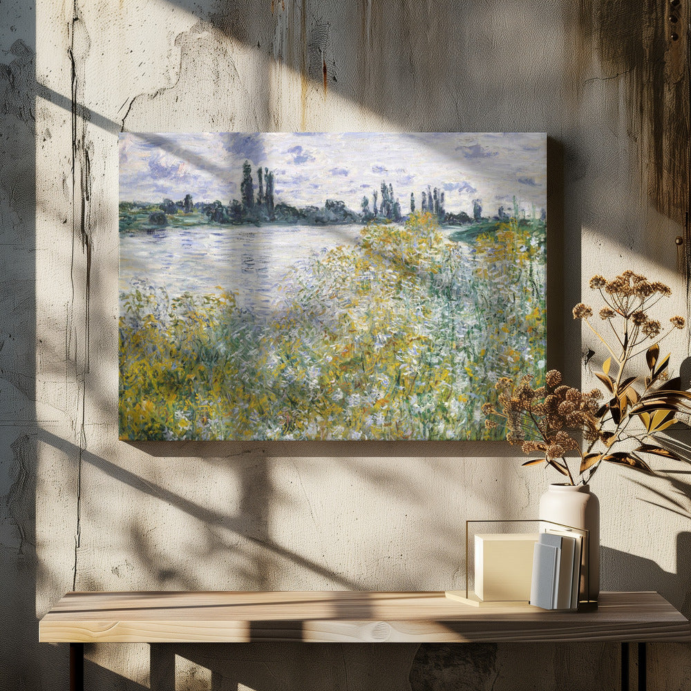 An impressionist landscape painting of a riverbank covered in yellow and white wildflowers. A calm river reflects the cloudy sky, and the opposite bank is lined with tall, dark poplar trees. The artwork is displayed in a silver frame. Artwork