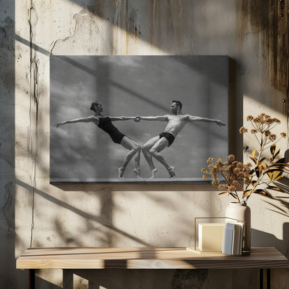 A black and white photograph of a male and female ballet dancer striking a symmetrical, athletic pose on a ledge. They hold hands, leaning away from each other in a display of strength and balance against a cloudy sky, all enclosed within a silver frame. Print