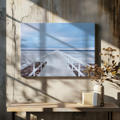 A framed photograph capturing a long, white wooden pier from a central perspective, leading the eye across a calm, icy sea towards the distant horizon under a cloudy blue sky. Print