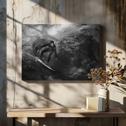 A dramatic black and white photograph of a surfer in a wetsuit skillfully riding down the face of a large, turbulent wave. The image is enclosed in a silver frame. Wall Art
