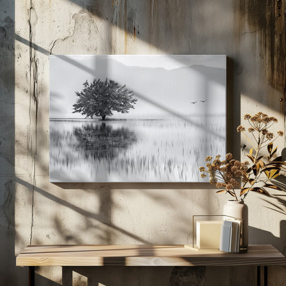 A serene black and white landscape photograph of a solitary tree standing in a calm lake, its reflection mirrored perfectly in the water. Hazy mountains are visible in the distance, and two birds fly across the pale sky, all enclosed within a silver frame. Print