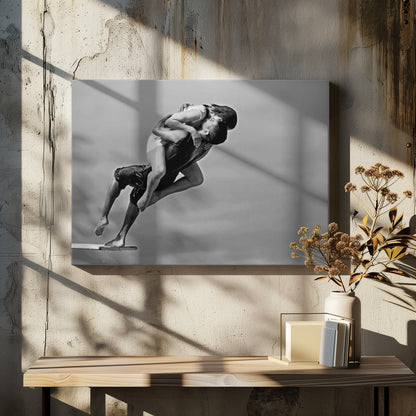 A framed, black and white photograph capturing a dynamic and romantic moment. A man is leaping off a diving board, carrying a woman who is wrapped around him in a passionate embrace, their faces close together. The background is a simple, plain gray, emphasizing their mid-air pose. Wall Art
