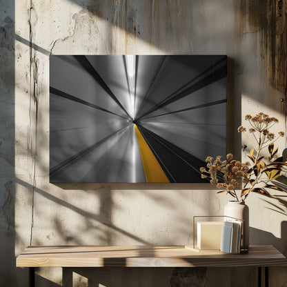 An abstract, long-exposure photograph from a first-person perspective inside a tunnel, creating a motion-blurred effect. The scene is mostly black and white, with lines radiating from a central vanishing point, but a single, bold yellow line runs down the center, adding a pop of selective color. The artwork is presented in a silver frame. Print