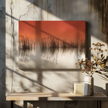 A minimalist landscape photograph in a silver frame, showing dark reeds silhouetted against a vibrant solid orange sky. The calm water perfectly reflects the reeds and the warm glow of the sky, creating a serene and abstract scene. Print