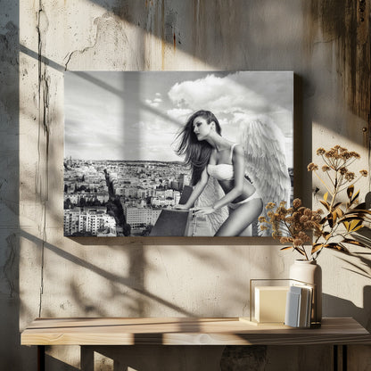 A framed black and white photograph of a woman with large angel wings wearing white lingerie, looking out over a cityscape from a high vantage point. Her long dark hair is blowing in the wind, and the sky is filled with clouds. Poster