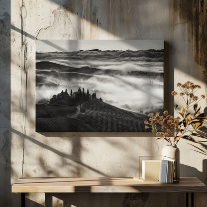 A framed, black and white photograph of a dramatic Tuscan landscape. A villa surrounded by cypress trees sits on a foreground hill, while thick fog blankets the rolling hills and valleys below. In the distance, a sea of clouds stretches towards a mountain range. Wall Art