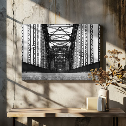 A framed, black and white, low-angle photograph capturing the symmetrical and intricate steel truss structure of a long bridge, creating a powerful vanishing point perspective down the center of the road. Poster