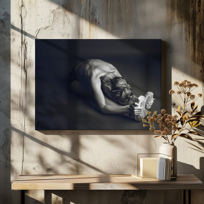 A black and white photograph of a ballerina stretching. She is seated on the floor in a deep forward fold, her torso bent over her legs as she holds onto her pointe shoes. The lighting accentuates the musculature of her back and shoulders, and her hair is styled in a braided bun. Decor