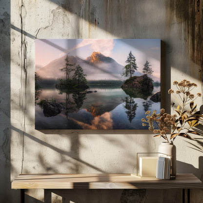 A serene mountain lake at sunrise or sunset, with a prominent peak illuminated by golden light. Small, rocky islands with pine trees dot the calm, clear water, which perfectly reflects the sky, trees, and mountains. A light mist hangs over the water and around the base of the mountains in the background. Decor