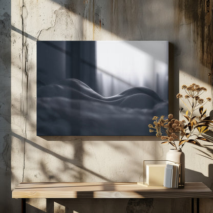 A close-up black and white artistic photograph capturing the soft curves of a person's back and hips as they lie down. The background is softly lit by a window, creating a play of light and shadow that emphasizes the human form's abstract, sculptural qualities. The image is displayed in a silver frame. Print