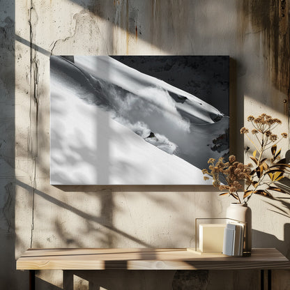 A dramatic black and white photograph of a skier speeding down a steep, snow-covered mountain, kicking up a large cloud of powder. The image is framed with a brushed silver border. Decor