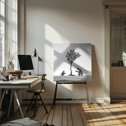 A framed, black and white photograph depicting a surreal scene of a man and a child sitting on toilets in an open grassy field under a single tree, both wearing hats and reading. Print