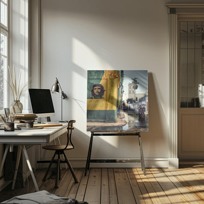 A framed photograph of a vibrant street corner in a city like Havana, Cuba, with a large mural of Che Guevara on a yellow and green wall. The wet street reflects the buildings and a palm tree, while people, a vintage car, and a rickshaw occupy the narrow road. Poster