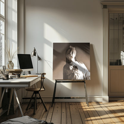 A framed, sepia-toned photograph of a classical marble bust of a woman. She looks upwards and to the side, illuminated by a strong light that casts dramatic shadows across her face and draped clothing. The photo is enclosed in a simple, light wood frame. Print