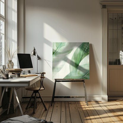 A light wood framed artwork depicting a close-up, abstract watercolor painting of large, overlapping tropical leaves. The shades of green are soft and translucent, creating a layered effect against a bright white background, evoking a sense of calm and nature. Print