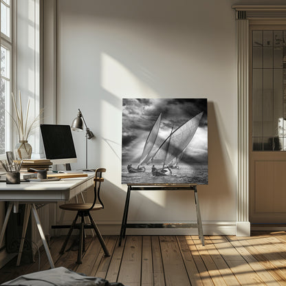 A dramatic black and white photograph of a fleet of traditional wooden sailboats with large, billowing sails racing on a choppy sea under a dark, stormy sky. The image is presented in a light wood frame. Print