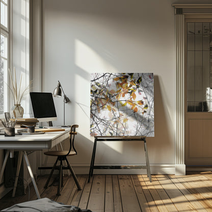 An abstract artwork in a light wood frame featuring a dense tangle of black and grey branches interwoven with soft, glowing autumn leaves in shades of orange and yellow against a white background. Poster