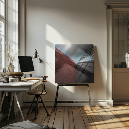 A dramatic low-angle photograph of two modern buildings with contrasting facades. On the left, a building is covered in deep red square panels. On the right, a darker building features black angular tiles and glass windows. The sky above is a moody, blurred grey. Print