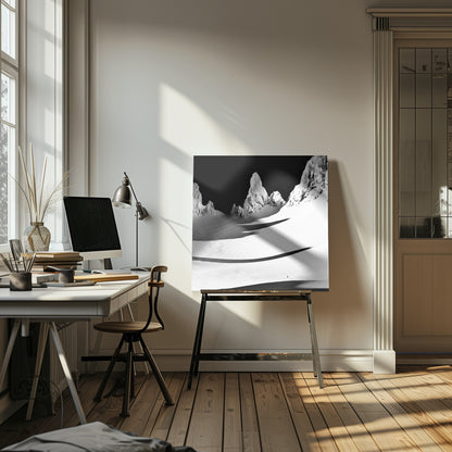 A framed, high-contrast black and white photograph of a majestic, snow-covered mountain range. Jagged peaks are sunlit against a stark black sky, casting long, dramatic shadows across a vast, pristine snowfield below. A tiny, solitary figure stands in the snow, highlighting the immense scale of the landscape. Print