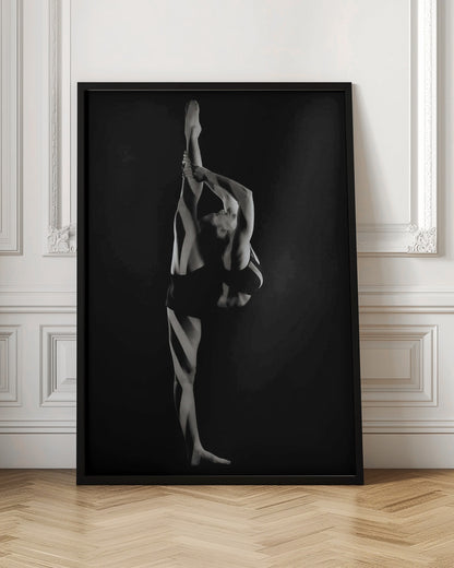 A dramatic black and white studio photograph of a female dancer performing a standing split. She balances on one leg while holding the other leg straight up vertically next to her head, arching her back and looking upwards. The strong side lighting creates a chiaroscuro effect, highlighting her musculature and form against a solid black background. Print