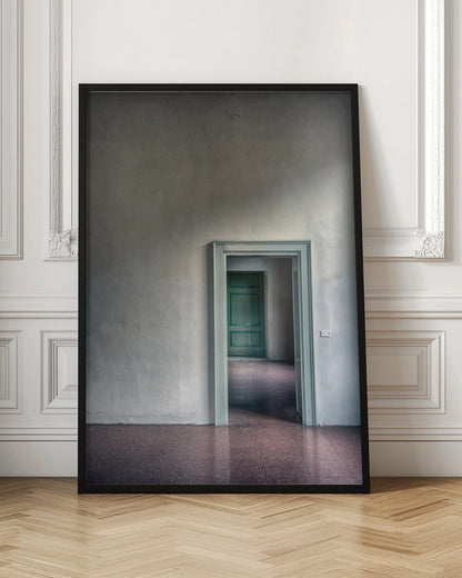 A minimalist photograph of a room with grey, textured walls and a reddish-brown floor, focusing on an open, light green doorway that reveals another room with a closed, darker green door, creating a sense of depth and perspective. Wall Art