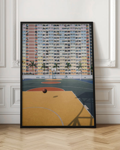 A vibrant photograph of a basketball court with a yellow and green floor, a single basketball is mid-bounce in the foreground. In the background stands the massive, symmetrical Choi Hung Estate apartment building in Hong Kong, famous for its facade of pastel rainbow colors. Palm trees line the space between the court and the building. Print