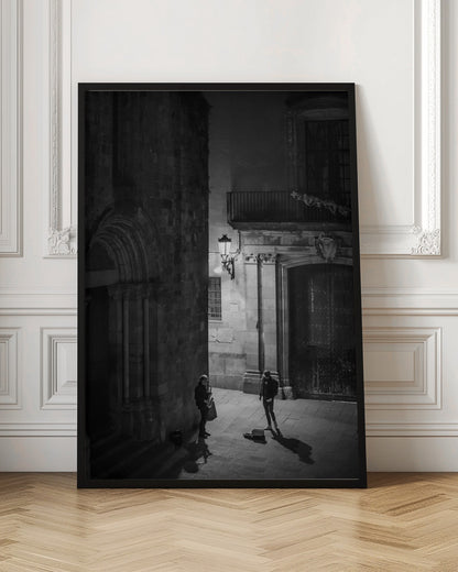 A high-angle, black and white photograph of a street musician playing a saxophone for a lone listener in a narrow stone alley at night. The scene is illuminated by an ornate streetlamp, casting long shadows on the cobblestone ground. Wall Art