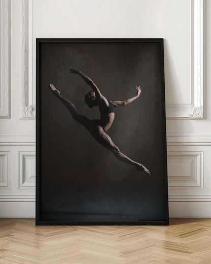 A dramatic, low-key studio photograph of a muscular female dancer captured mid-leap. She is in a full split, arching her back with her arms extended gracefully. The lighting accentuates her toned physique against a dark, textured brown background. Poster