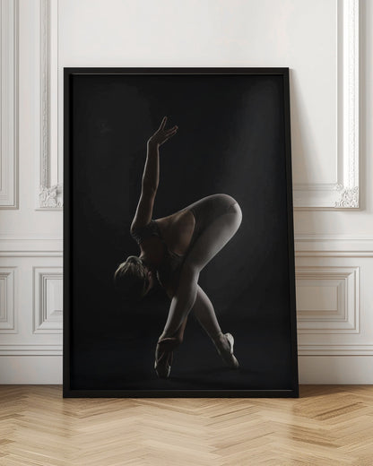 A dramatic studio photograph of a ballerina in a complex pose against a solid black background. Strong rim lighting highlights the graceful curves of her body as she bends forward with her legs crossed, one arm extended high and the other reaching towards her pointe shoes. Poster