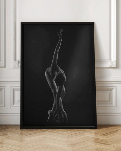 A dramatic black and white photograph of a ballerina posed against a dark background. She is bent forward at the waist, with her legs crossed and on pointe. One arm reaches up towards the ceiling in a graceful curve while the other hand touches the floor near her feet, showcasing her flexibility and strength. Wall Art