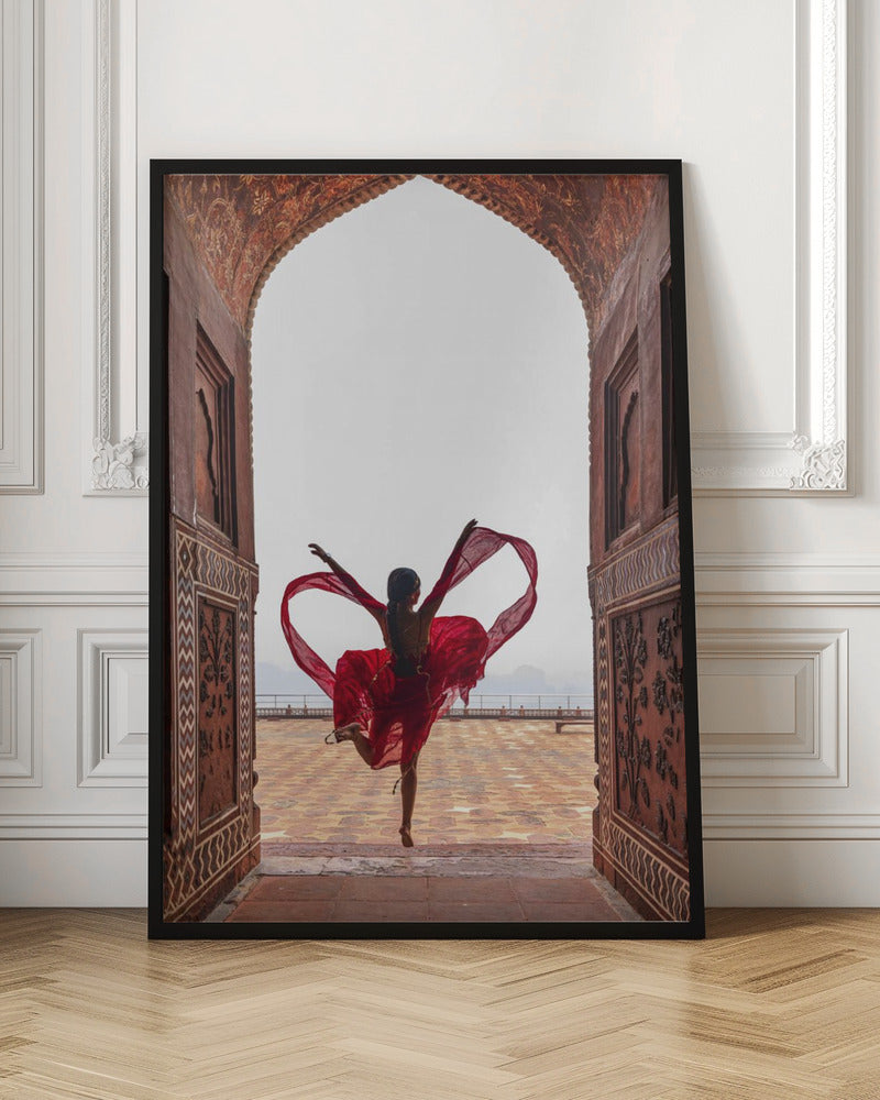 A woman in a flowing red dress dances joyfully, framed by an ornate, carved archway. Seen from behind, she leaps with her arms outstretched, holding a long red scarf that forms a heart shape around her against a bright, hazy sky. Poster