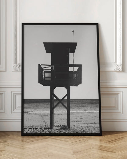 A high-contrast, black and white photograph of a silhouetted lifeguard tower standing on a sandy beach. The tower is centrally framed against a bright, empty sky, with the ocean and horizon visible in the background. Wall Art