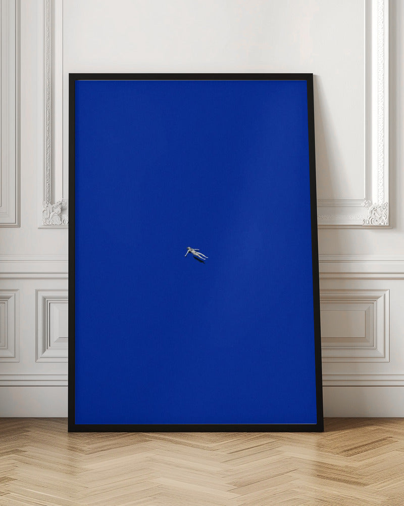 A minimalist and surreal artwork featuring a tiny, pale human figure floating peacefully in the center of an immense, solid, and vibrant blue void, all enclosed within a thin black frame. Wall Art