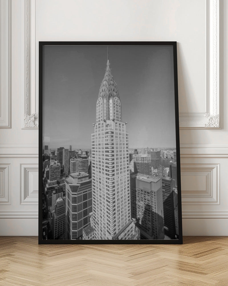 A high-angle, black and white photograph of the iconic Chrysler Building, its Art Deco spire prominently featured against the New York City skyline under a clear sky. Artwork
