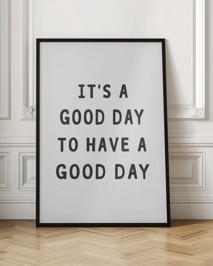A framed black and white art print with the phrase 'IT'S A GOOD DAY TO HAVE A GOOD DAY' in a bold, dark gray, sans-serif font. Artwork