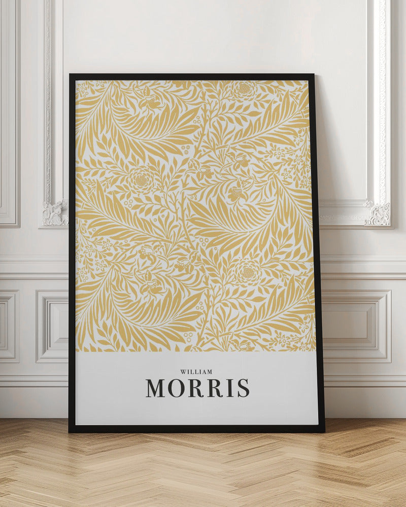 A framed exhibition-style poster of a William Morris design. The poster features an intricate, golden-yellow floral and leaf pattern on a white background. Below the pattern, the name 'WILLIAM MORRIS' is printed in black text. The entire artwork is presented in a simple black frame. Wall Art