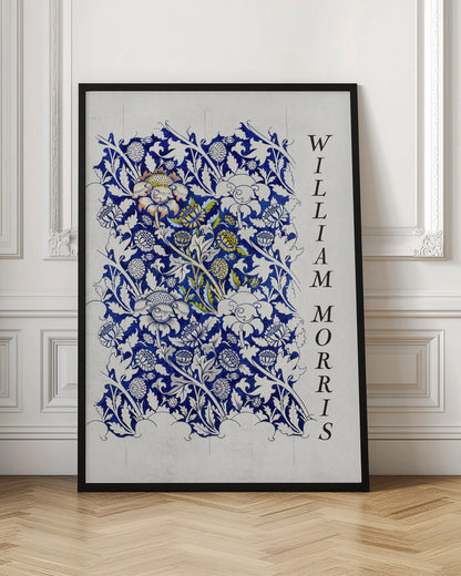 A vintage art print by William Morris featuring an intricate blue and white floral pattern on a light gray, textured background. The design swatch shows stylized flowers and acanthus leaves, with some central flowers highlighted in yellow and peach. The name 'WILLIAM MORRIS' is printed vertically in a black serif font along the right edge. The print is displayed in a thin black frame. Decor